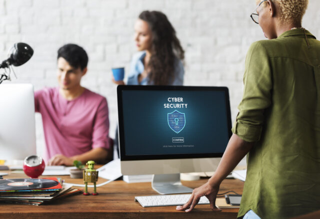 A team works in the office with protected laptops, showcasing the importance of having a fine balance between cybersecurity and remote working.