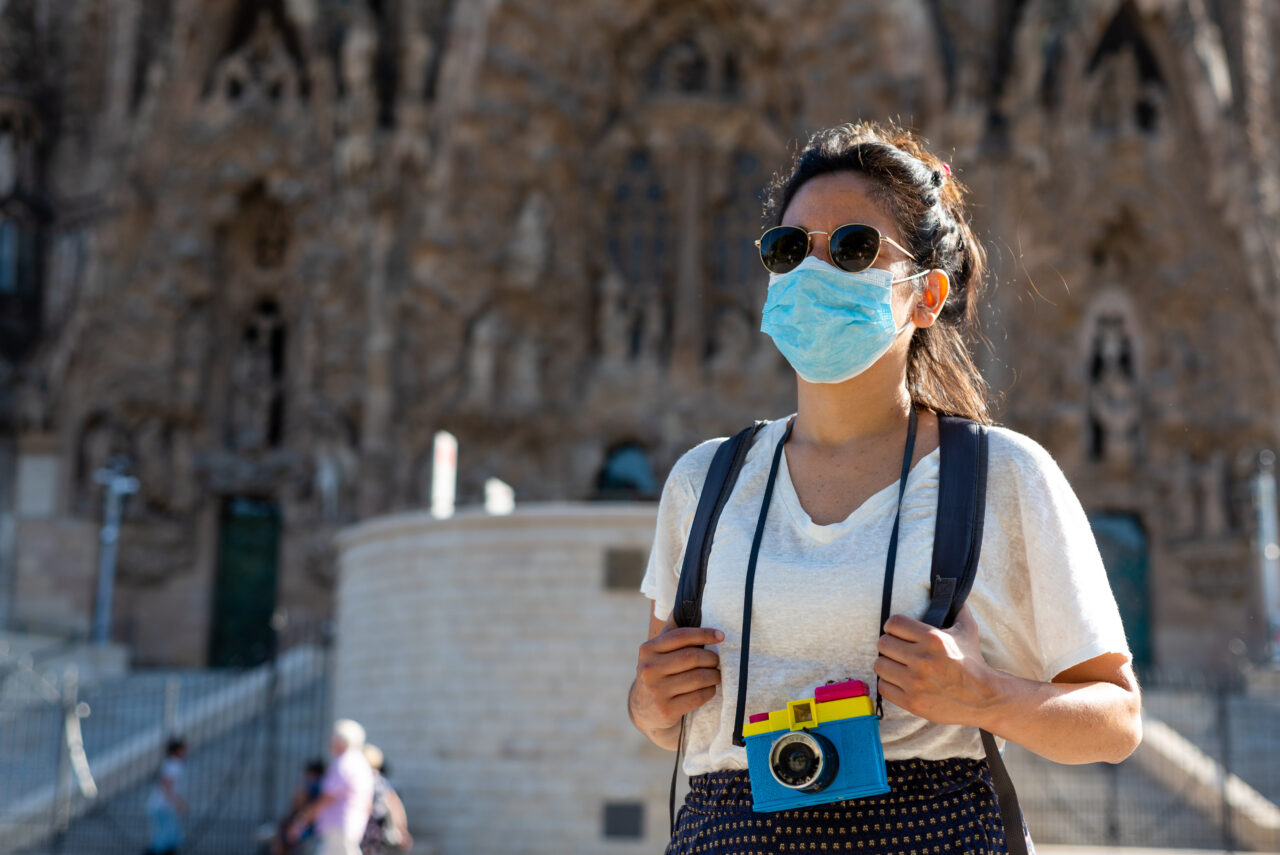 A traveller walks with a mask and eyeglasses.
