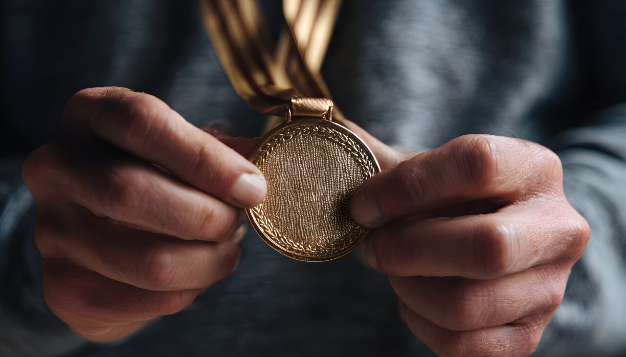 A close-up of hands holding a gold medal with a ribbon. The medal symbolizes employee champions