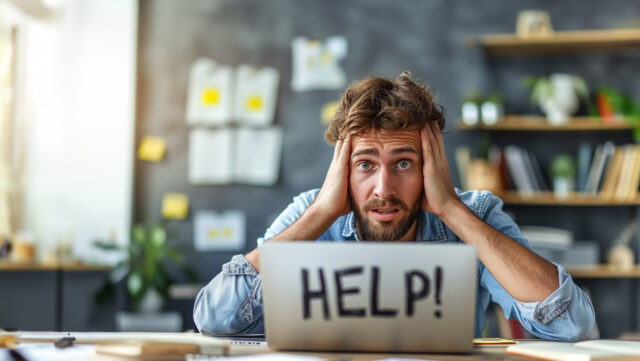 A man is sitting at a desk with a laptop open and the word HELP written on it. Symbolising job hugging trend.